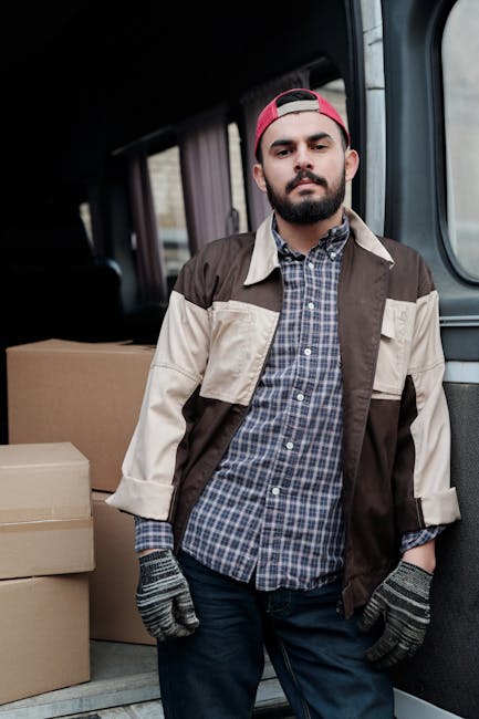 A man and woman standing beside an open moving van during a home relocation, with the man taking notes on a clipboard while the woman holds a cardboard box. The van’s interior is filled with stacked